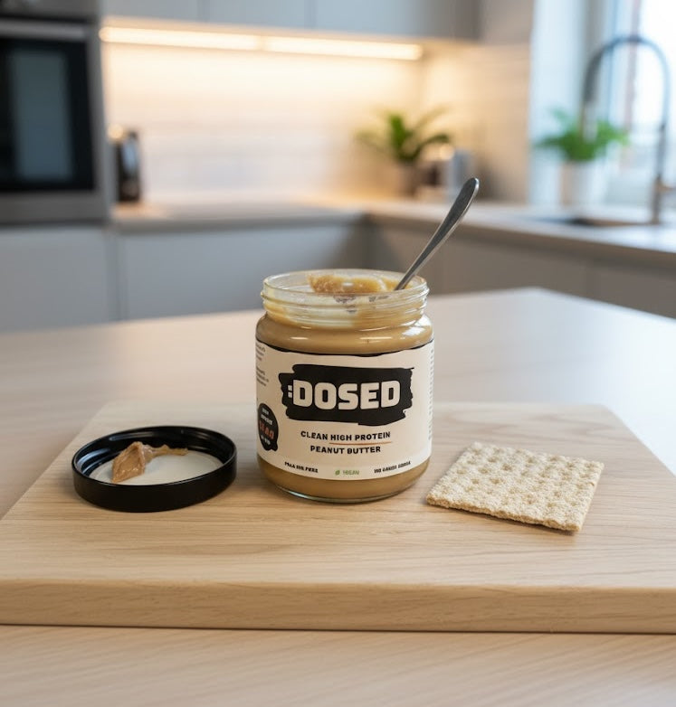 Jar of Dosed peanut butter on a kitchen counter with a spoon and crackers.